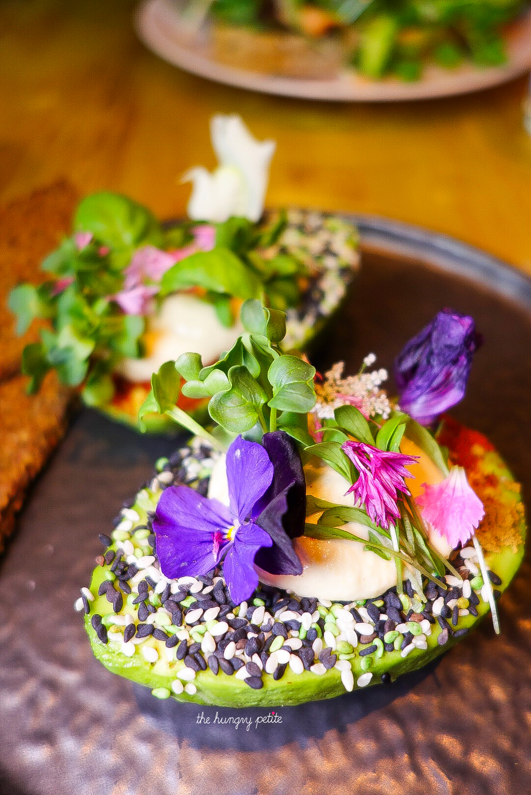 The Avo Garden - Two avocado halves filled with hummus, decorated with spices & flowers and sidekicked by crispy multigrain toast.